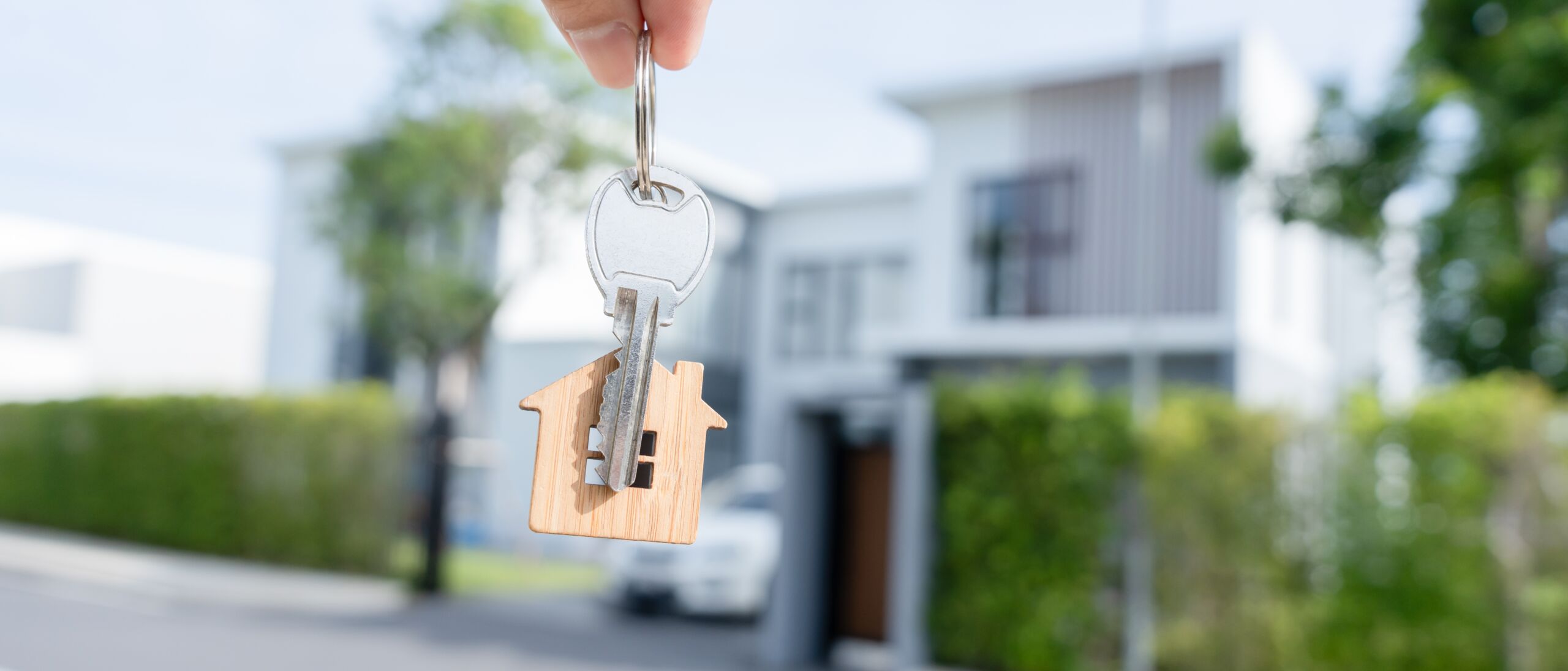 Page title background for Rental Management service: Hand holding keys with a house-shaped keychain in front of a modern home.